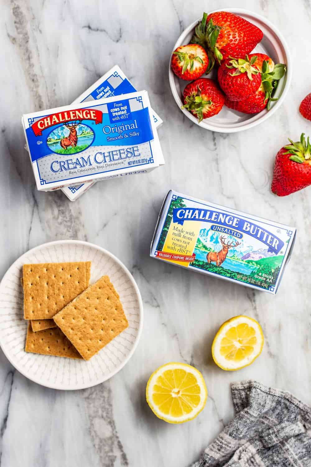 Ingredients for no-bake strawberry lemonade cheesecakes arranged on a marble countertop