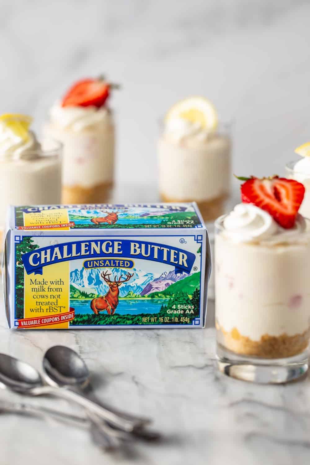 Mini no-bake strawberry lemonade cheesecakes next to a package of butter on a marble counter