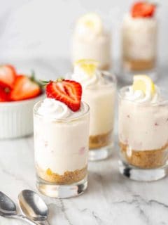 Shot glasses filled with creamy no-bake strawberry lemonade cheesecakes and topped with berries and lemons