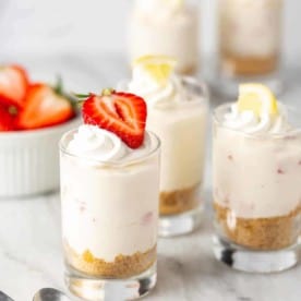 Shot glasses filled with creamy no-bake strawberry lemonade cheesecakes and topped with berries and lemons