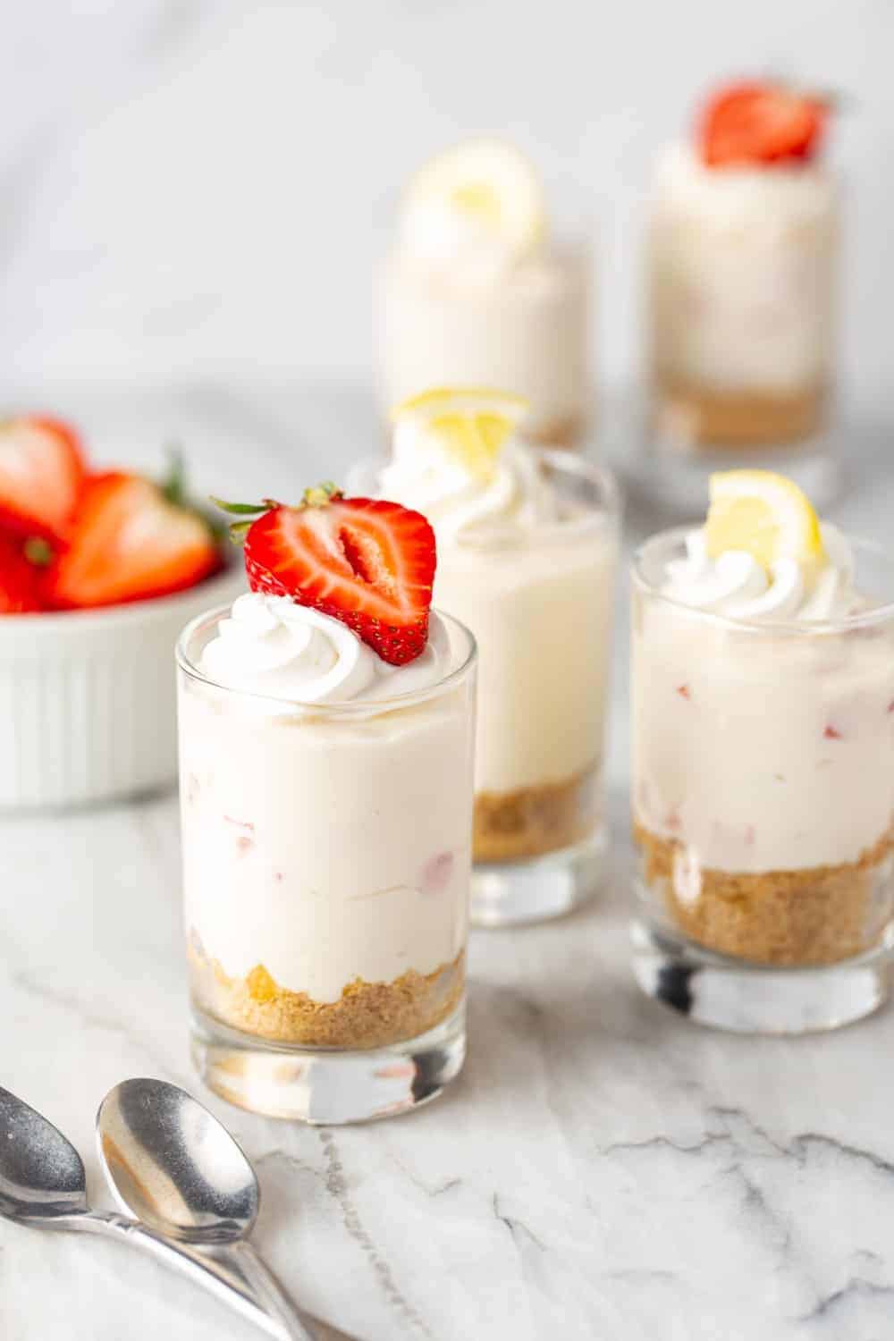 Shot glasses filled with creamy no-bake strawberry lemonade cheesecakes and topped with berries and lemons