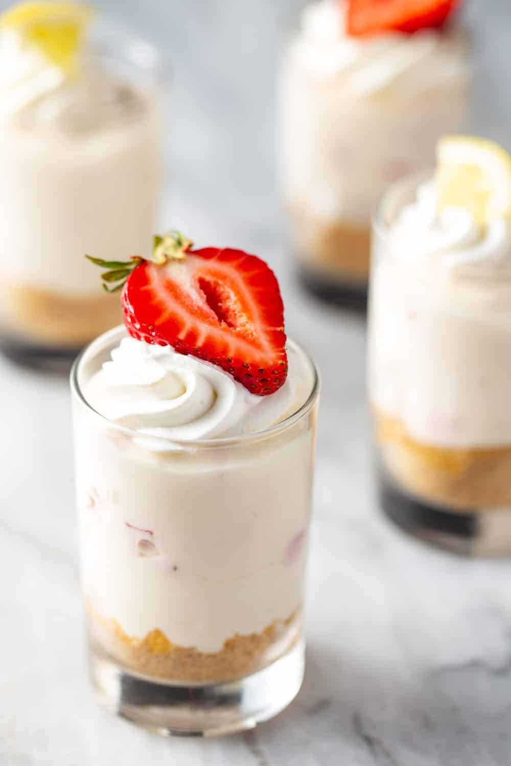 Close up of no-bake strawberry lemonade cheesecake in a shot glass, topped with whipped cream and a halved strawberry.