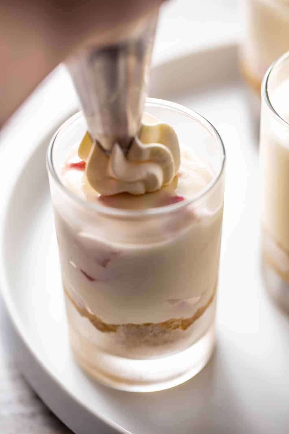 Piping bag piping whipped cream onto no-bake strawberry cheesecake in a shot glass