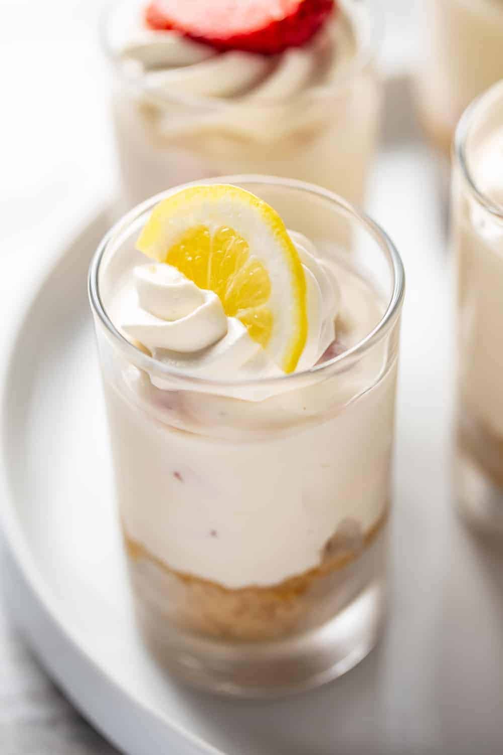 No-bake strawberry lemonade cheesecake in a small glass serving dish, topped with whipped cream and a lemon slice