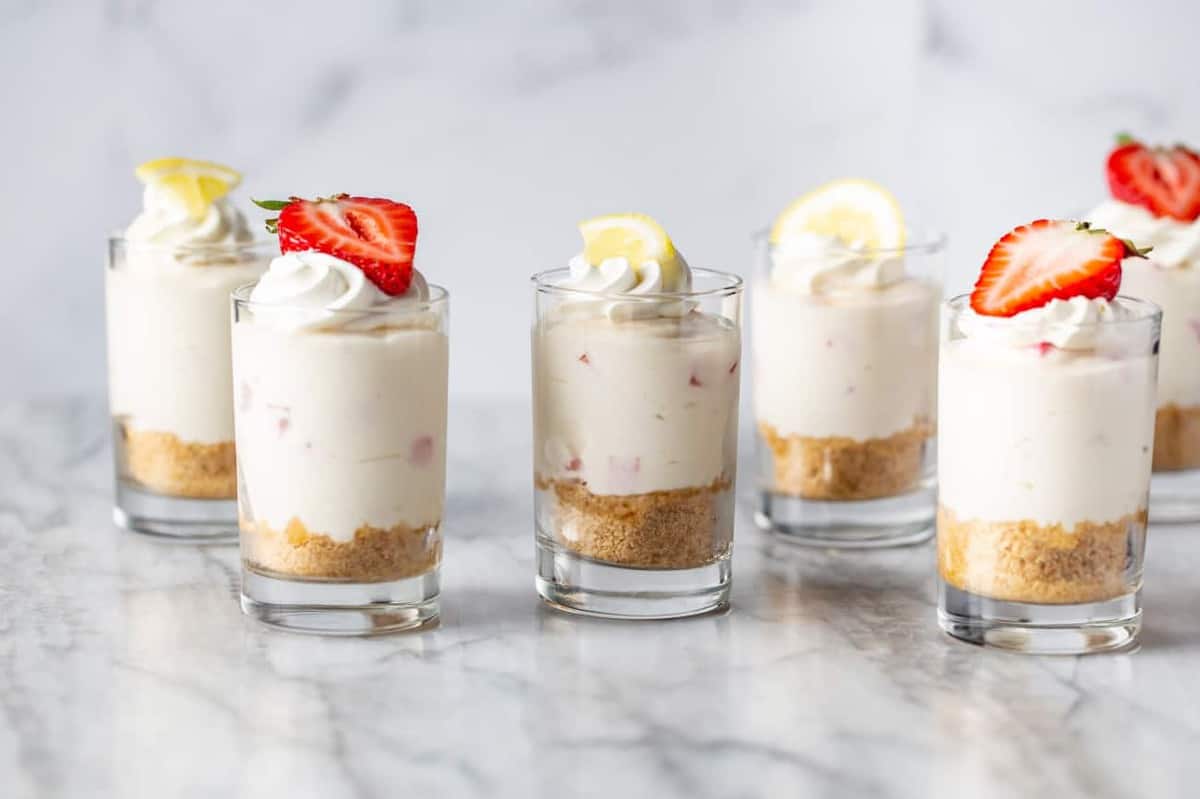 Dessert shot glasses filled with no-bake strawberry lemonade cheesecake arranged on a marble counter