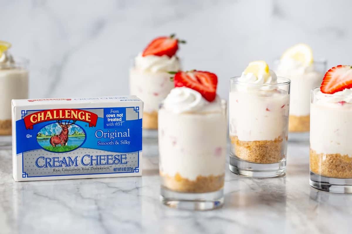 Mini no-bake strawberry lemonade cheesecakes next to a package of cream cheese on a marble counter