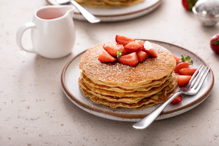 Stack of gluten-free pancakes topped with fresh strawberries on a plate.