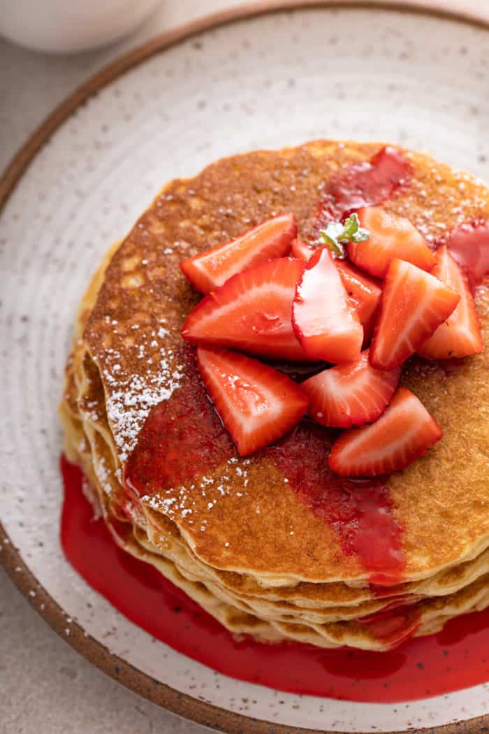 Stack of gluten-free pancakes topped with sliced strawberries and strawberry sauce.