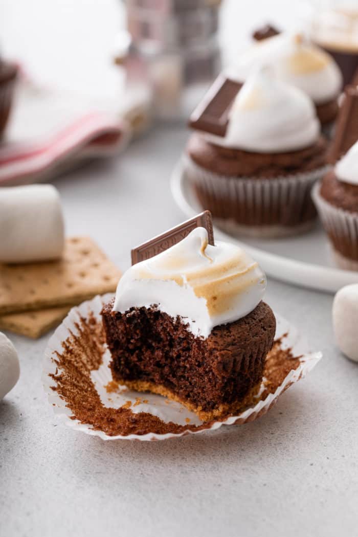 Unwrapped s'mores cupcake with a bite taken out of it. A platter of more cupcakes is visible in the background.