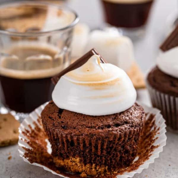 Unwrapped s'mores cupcake set on a gray countertop. A cup of espresso and more cupcakes are visible in the background.