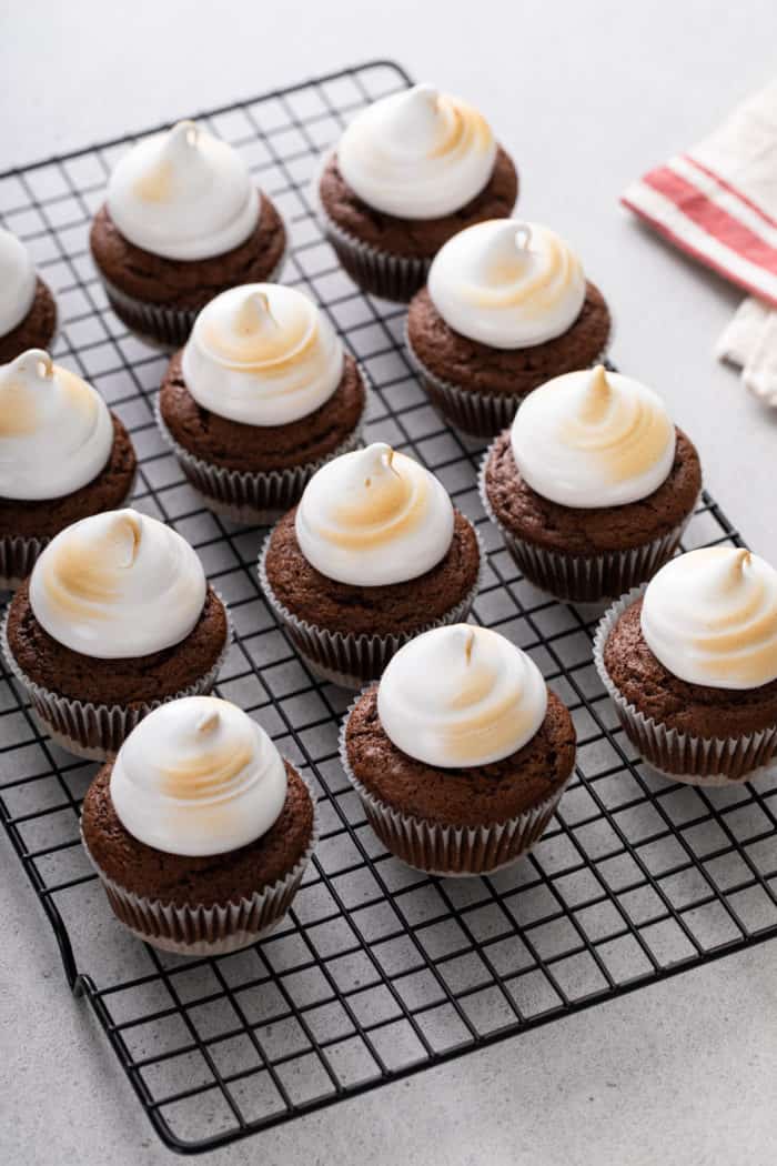 S'mores cupcakes topped with toasted marshmallow frosting lined up on a wire cooling rack.