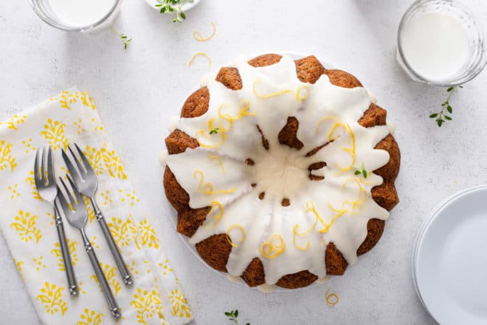 Overhead view of glazed lemon zucchini cake next to white plates and three forks.