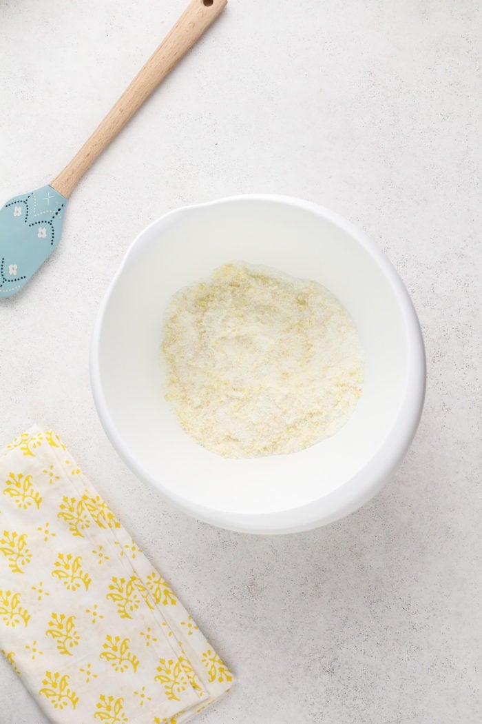 Lemon zest and granulated sugar mixed together in a large, white mixing bowl.