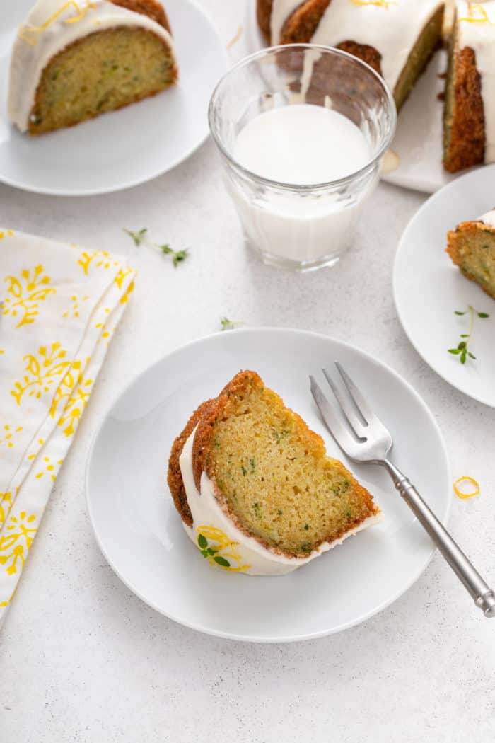 Three white plates, each holding a slice of lemon zucchini cake. A glass of milk is also visible on the countertop next to the plates.