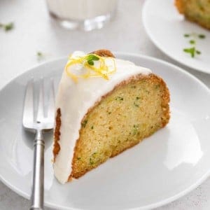 Slice of glazed lemon zucchini cake on a white plate.