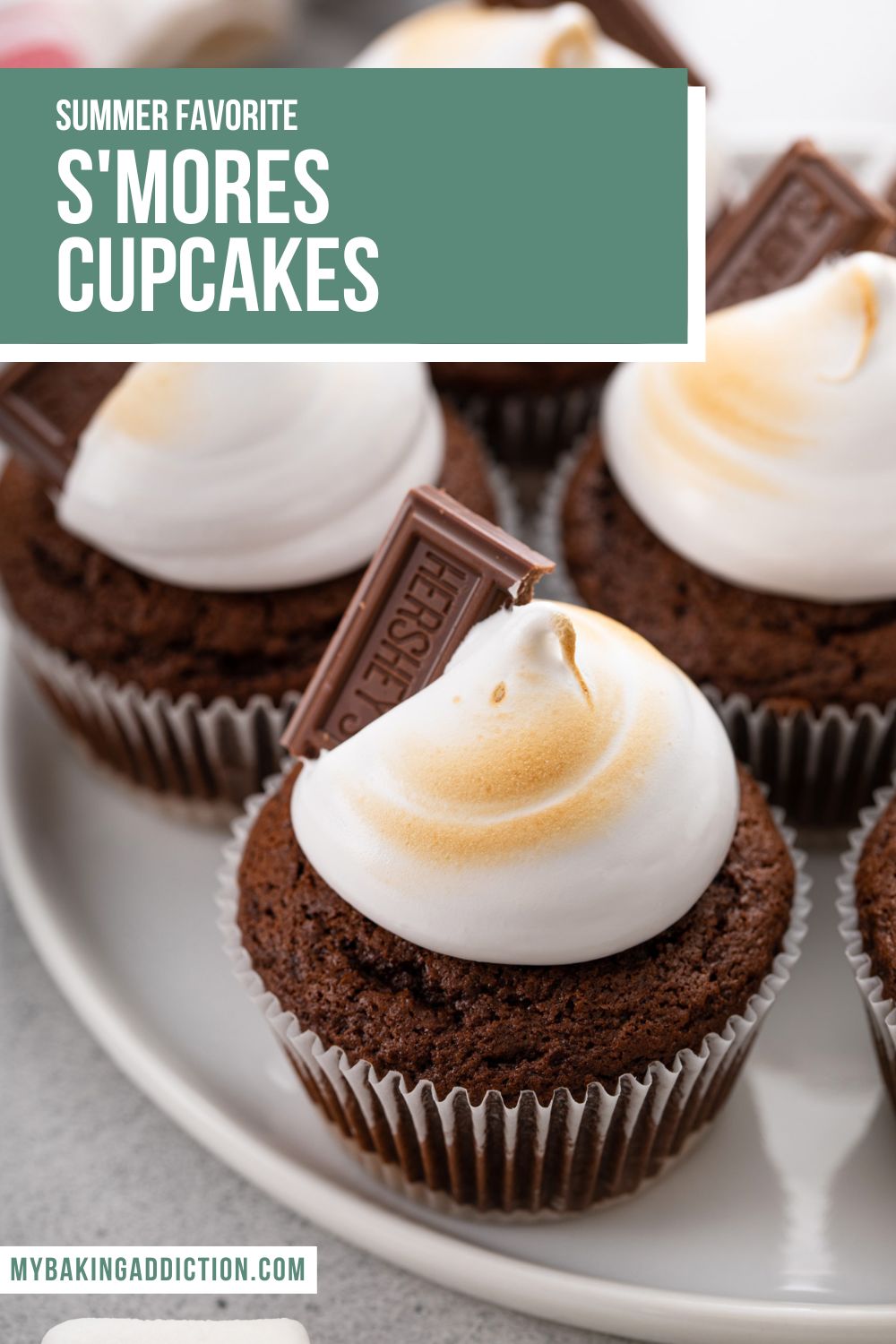 Close up of s'mores cupcakes topped with marshmallow frosting and a chocolate square on a white platter. Text overlay includes recipe name.