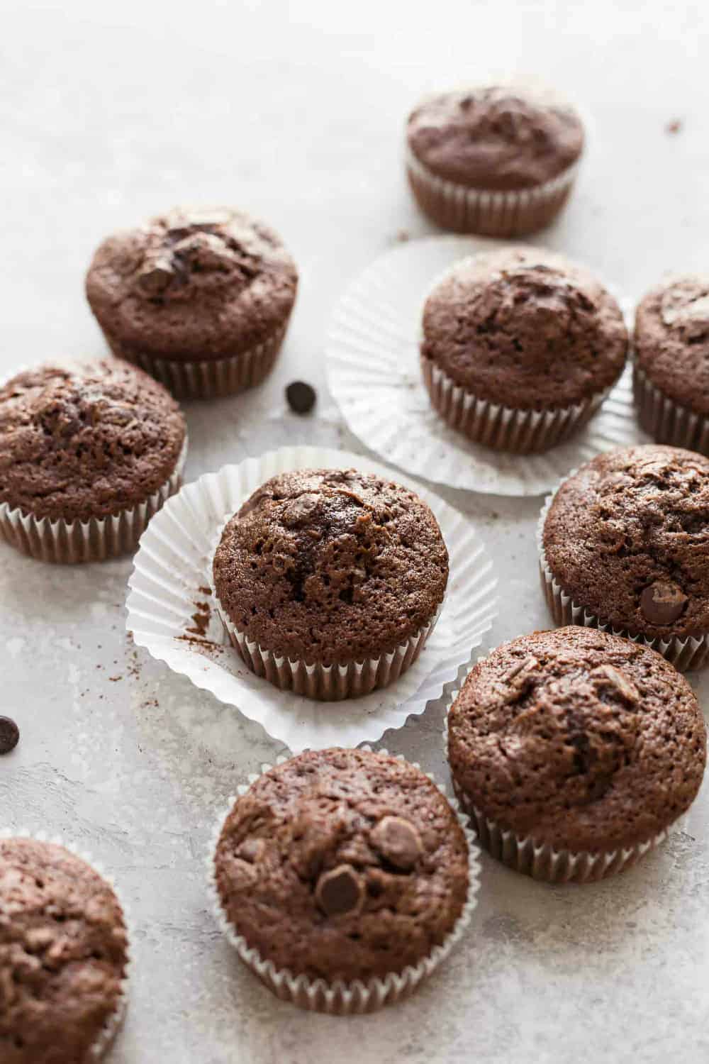 Baked chocolate zucchini muffins in white paper liners on a white surface