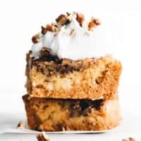 stacked pieces of pumpkin crunch cake with whipped cream and pecans