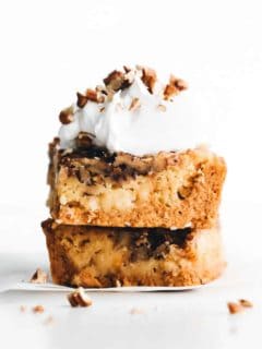 stacked pieces of pumpkin crunch cake with whipped cream and pecans