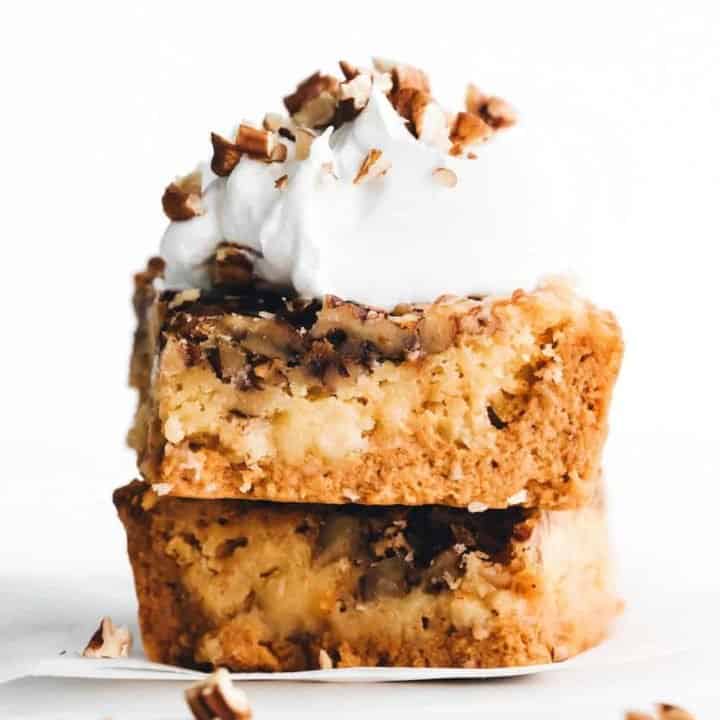 stacked pieces of pumpkin crunch cake with whipped cream and pecans