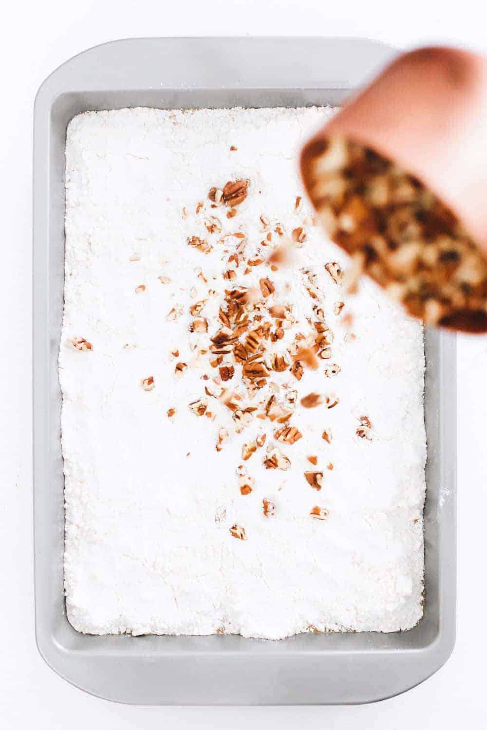 pumpkin crunch cake being topped with chopped pecans