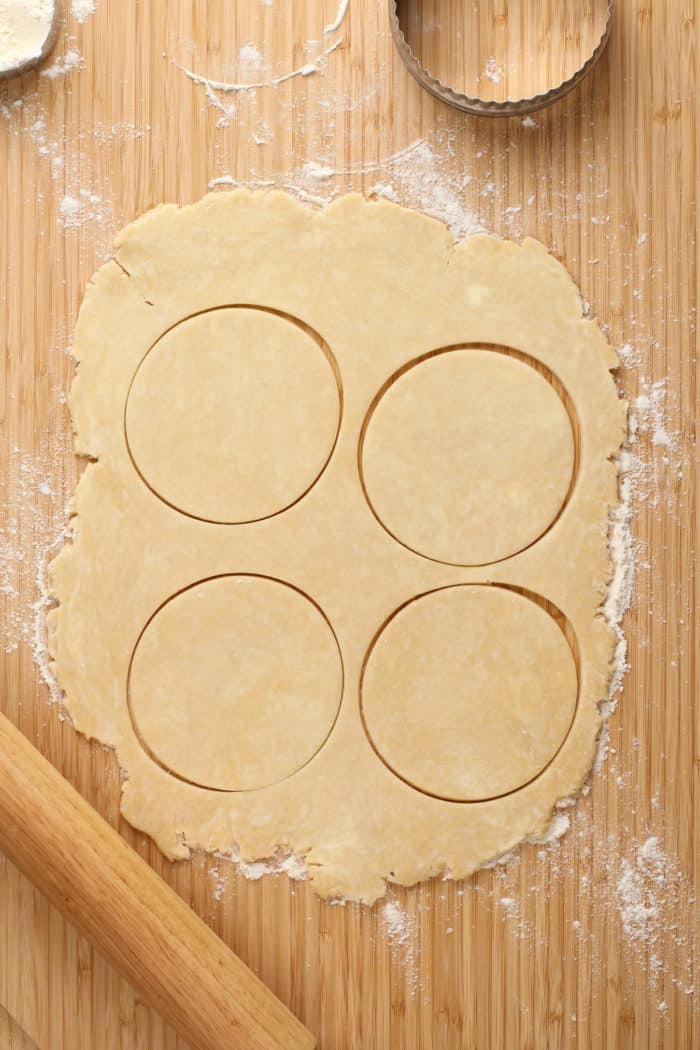 Pie dough rolled onto a wooden board and cut into four circles.