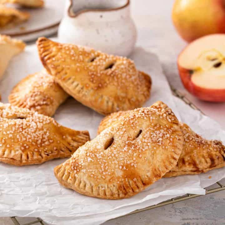 Baked apple hand pies scattered on parchment paper.