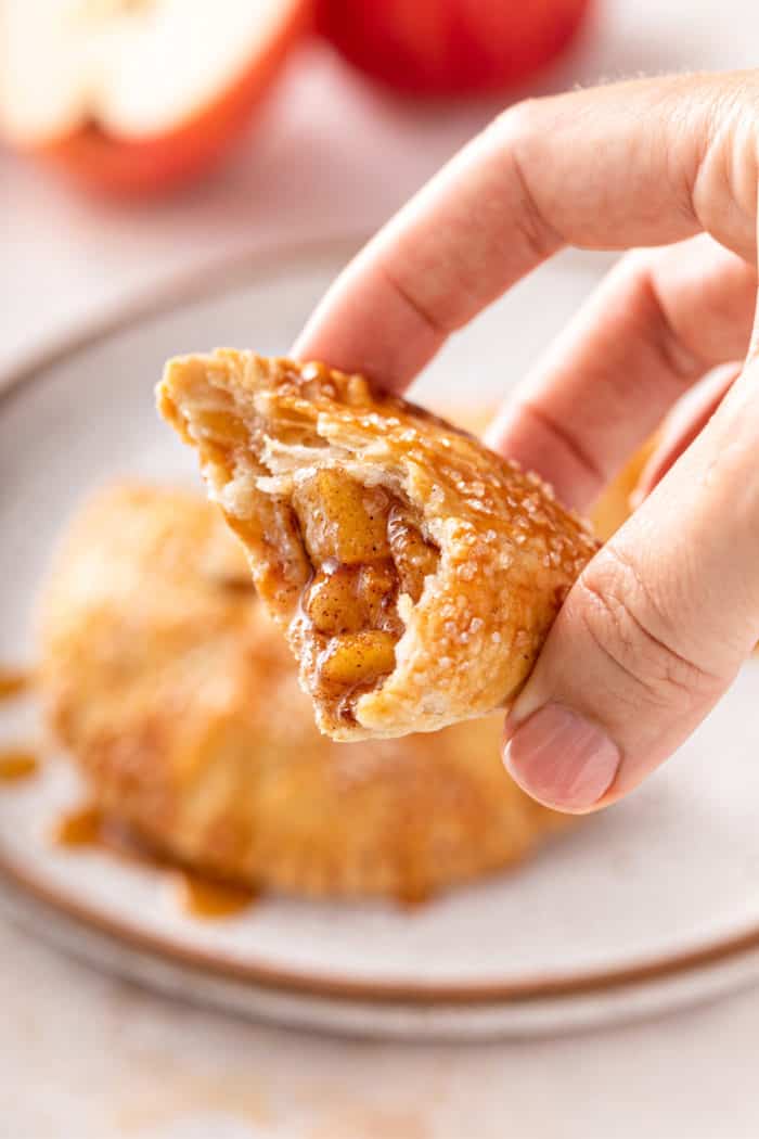 Hand holding up a halved apple hand pie to show the filling.