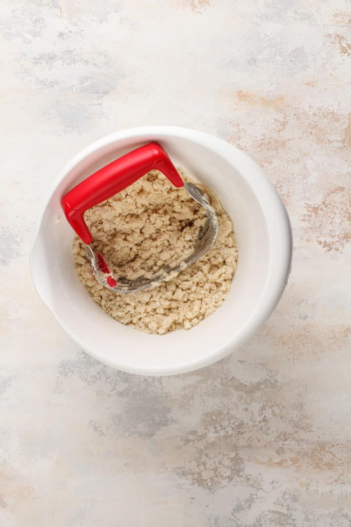 Pastry blender cutting butter into pie dough in a white mixing bowl.