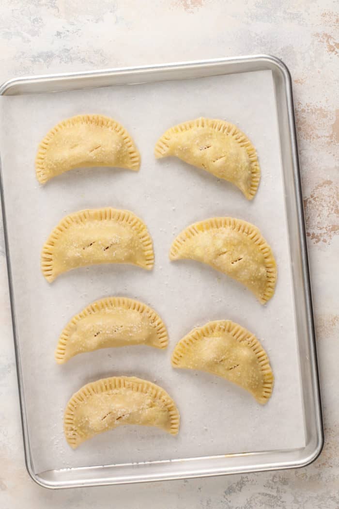 Unbaked apple hand pies on a piece of parchment paper on a baking sheet.