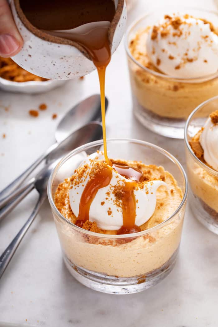 Caramel sauce being drizzled over no-bake pumpkin cheesecake in a glass dish.