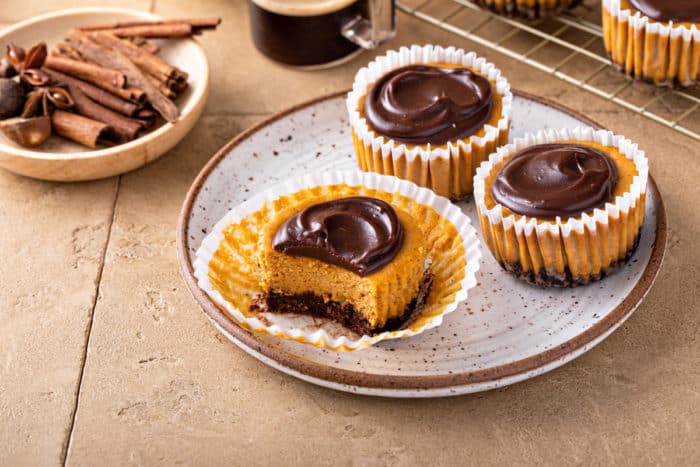 Three mini pumpkin cheesecakes on a plate. One of them is unwrapped and has a bite taken out of it.