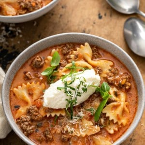 Close up of lasagna soup in a white bowl, topped with a spoonful of ricotta cheese