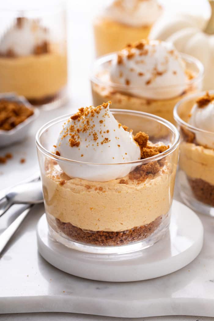 Glass dish filled with no-bake pumpkin cheesecake set on a white coaster.