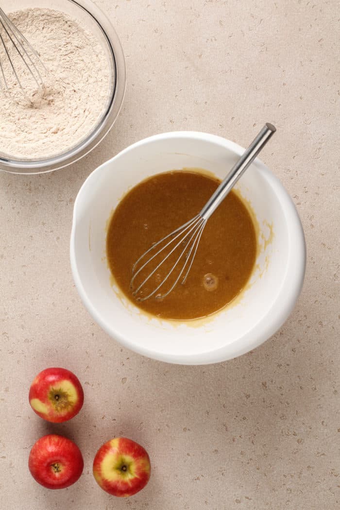 Bowl of dry ingredients set next to a white mixing bowl with wet ingredients for caramel apple cake.