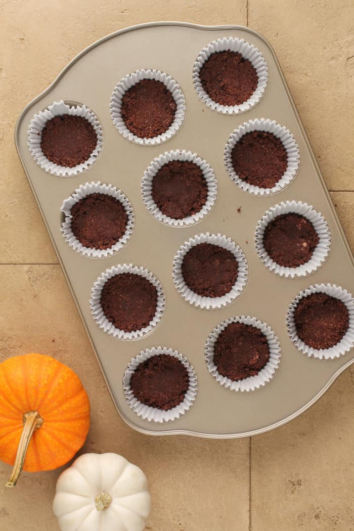 Mini chocolate crusts in a lined cupcake pan.