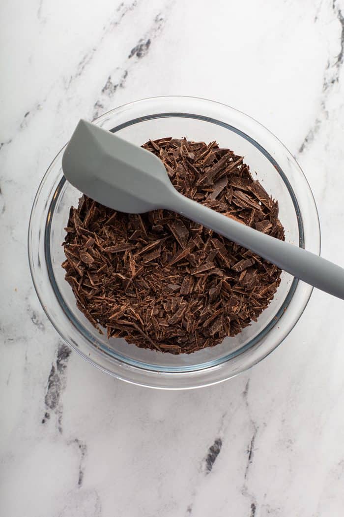 Gray spatula set on the edge of a glass mixing bowl filled with chopped chocolate