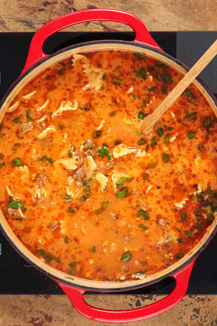 Wooden spoon stirring lasagna soup in a red dutch oven