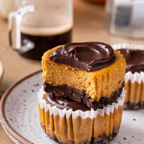 Two stacked mini pumpkin cheesecakes. The top one is unwrapped and has a bite taken out of it.