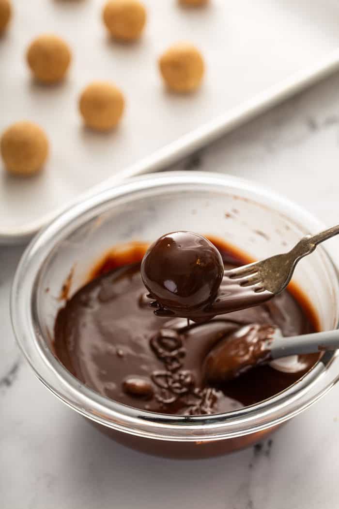 Fork holding a dipped turtle cookie ball over a bowl of melted chocolate