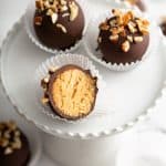 Three turtle cookie balls on a white plate, with one cookie ball bit in half to show the inside