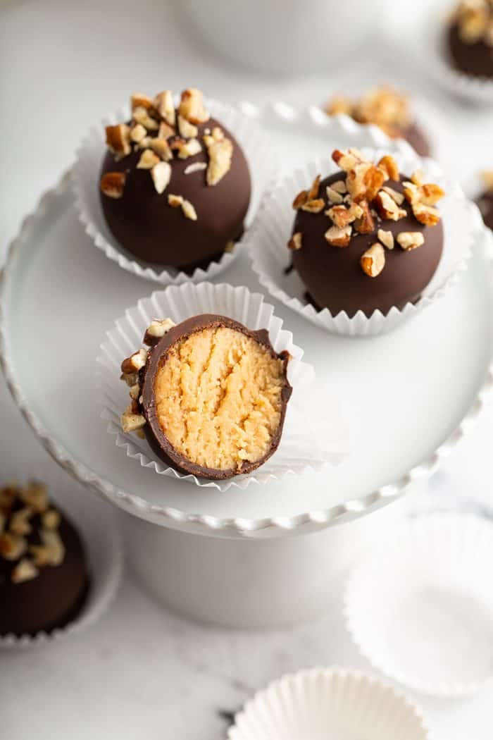 Three turtle cookie balls on a white plate, with one cookie ball bit in half to show the inside