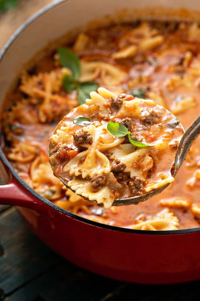 Ladle scooping up lasagna soup from a red dutch oven full of soup