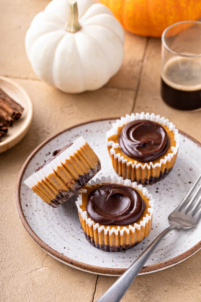 Three mini pumpkin cheesecakes, each topped with chocolate ganache, arranged on a plate.