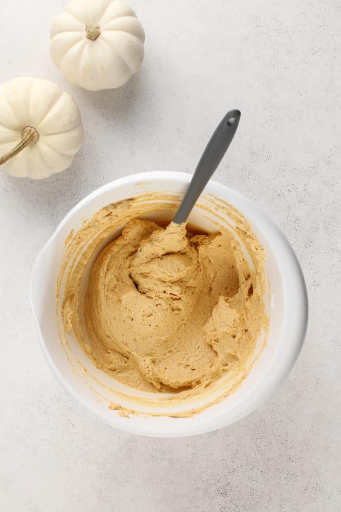 No bake pumpkin cheesecake being stirred together with a spatula in a white mixing bowl.