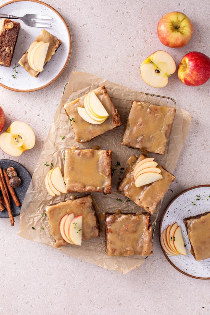 Overhead view of six slices of frosted caramel apple cake, garnished with thinly sliced apples.