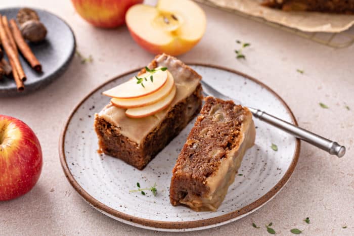 Two thin slices of caramel apple cake on a speckled plate. One of the pieces is turned on its side.