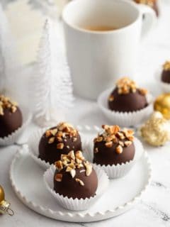 White plate with 3 turtle cookie balls in front of a cup of coffee
