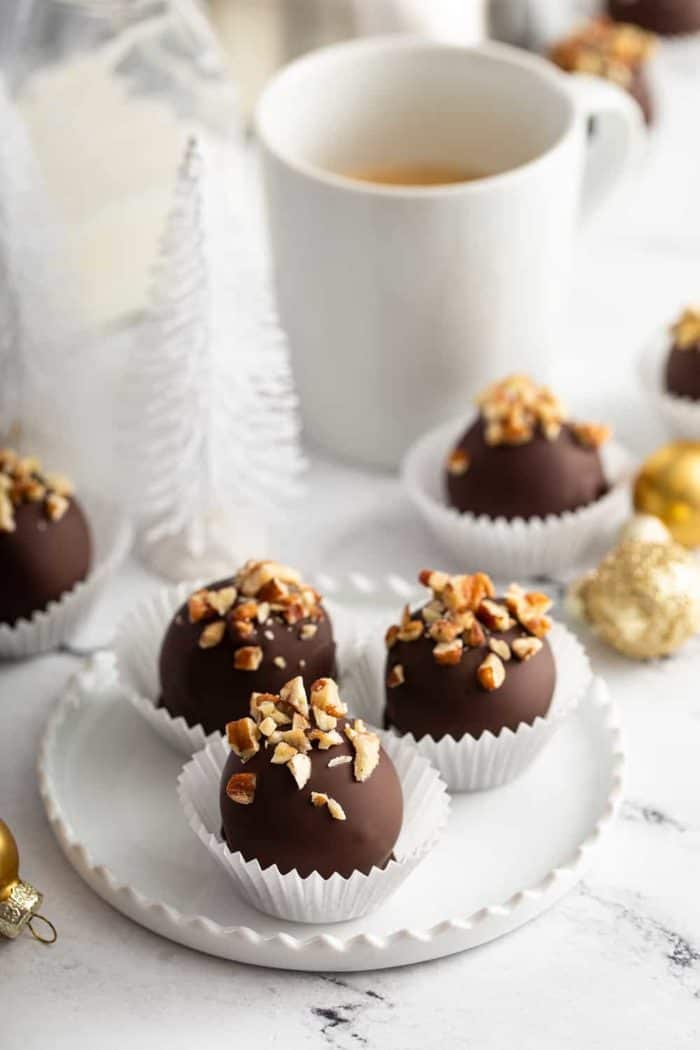 White plate with 3 turtle cookie balls in front of a cup of coffee