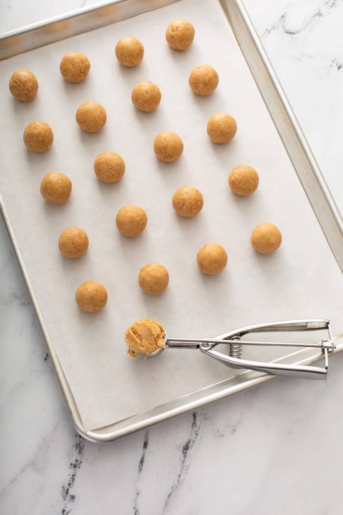 shaped cookie balls lined up on a parchment-lined baking sheet, ready to dip into chocolate